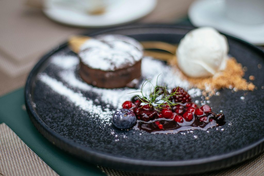 pexels-photo-9976033-9976033 Close-up of a gourmet dessert with chocolate, berries, and ice cream on a black plate.